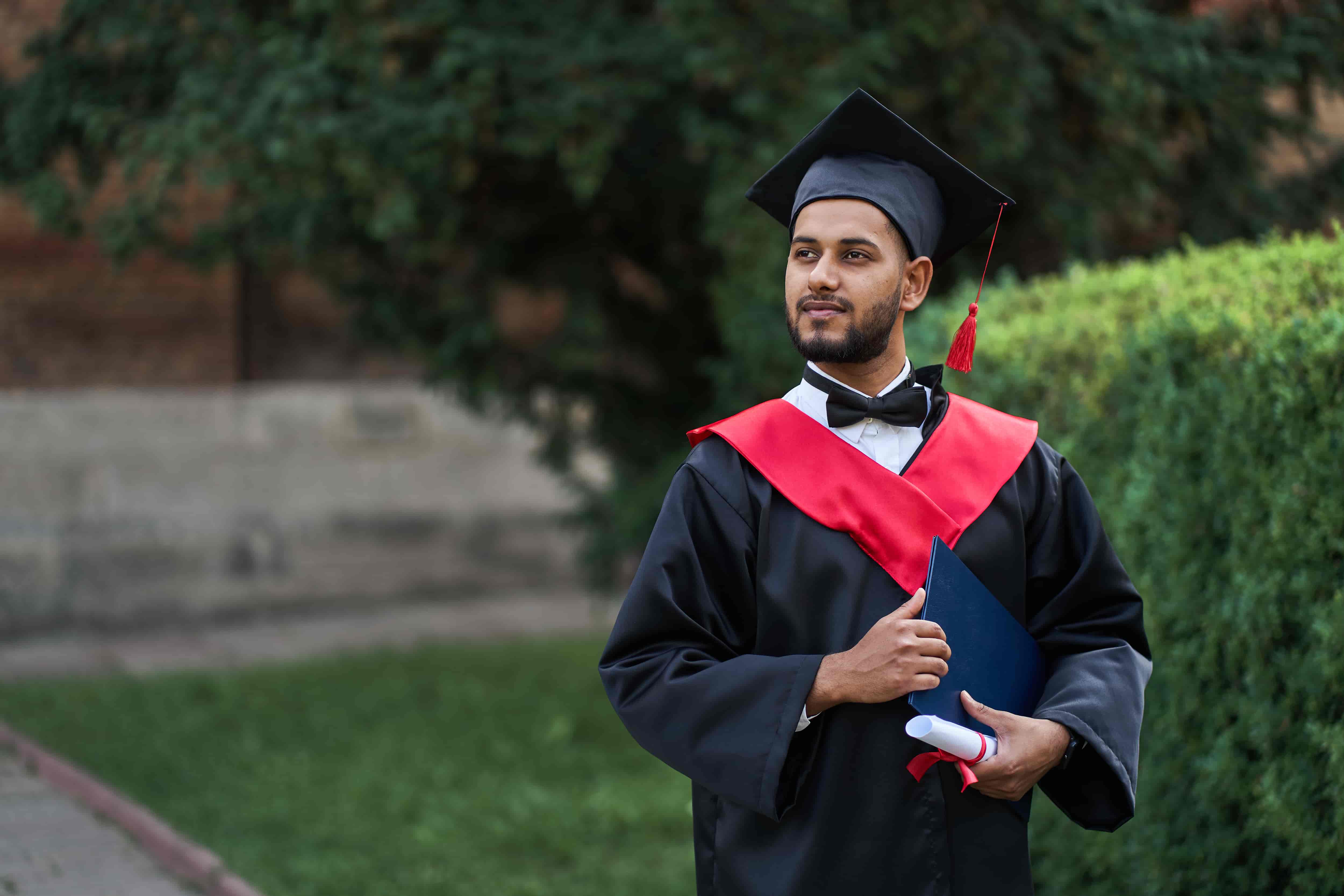 Indian graduate in graduation robe with diploma in university campus copy space