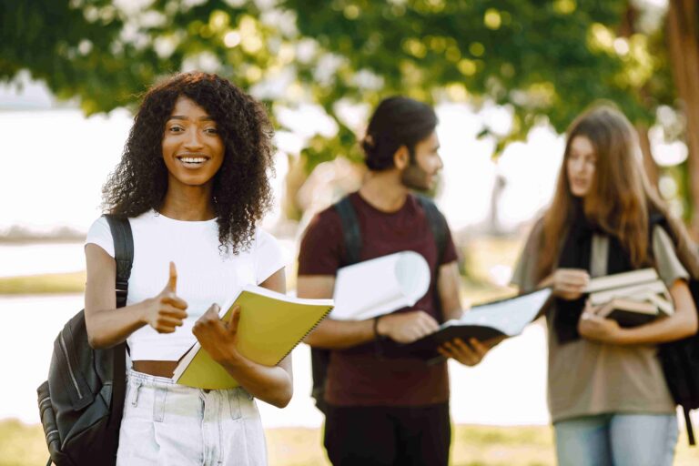 Three international students standing in a park and holding a bo