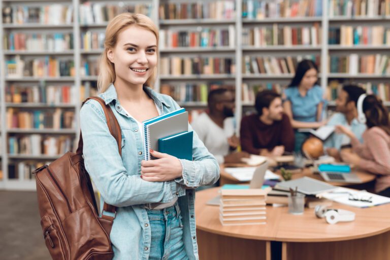 Group of ethnic multicultural students in library. White girl with notebooks